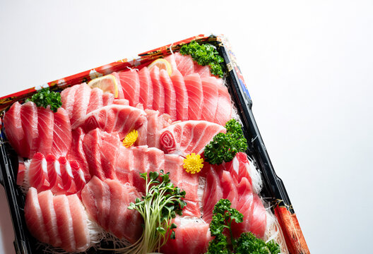 Premium assorted tuna sashimi platter including otoro and chutoro in a takeout bento box, white background with copy space