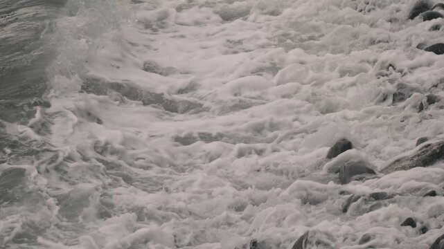 Waves crashing violently against numerous rounded stones along a rocky shore
