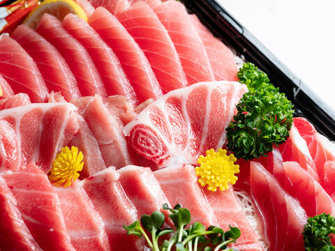 Premium assorted tuna sashimi platter including otoro and chutoro in a takeout bento box, white background with copy space