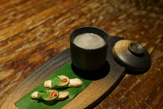 A glass of a unique cocktail "Khow Mun Kai (Thai Chicken Rice)" which is based on Thailand's food of the same name, served with chicken, cucumber, and chili inside a bar in Bangkok, Thailand, at night
