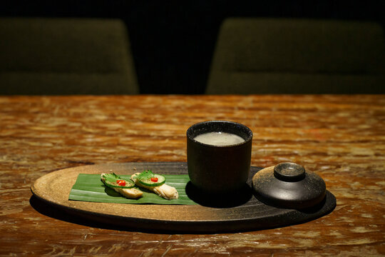 A glass of a unique cocktail "Khow Mun Kai (Thai Chicken Rice)" which is based on Thailand's food of the same name, served with chicken, cucumber, and chili inside a bar in Bangkok, Thailand, at night