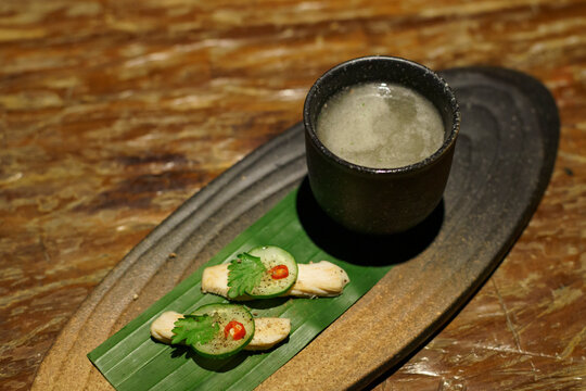 A glass of a unique cocktail "Khow Mun Kai (Thai Chicken Rice)" which is based on Thailand's food of the same name, served with chicken, cucumber, and chili inside a bar in Bangkok, Thailand, at night