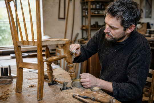 Furniture Craftsperson Restoring a Vintage Wooden Chair with Natural Wax in a Traditional Workshop Supporting Reuse and Material Conservation for Future Generations