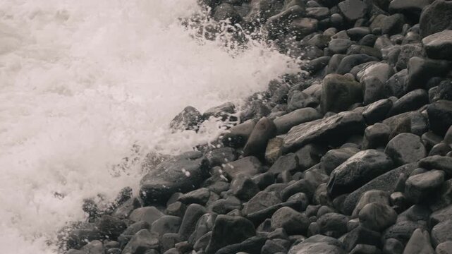Waves crashing violently against numerous rounded stones along a rocky shore
