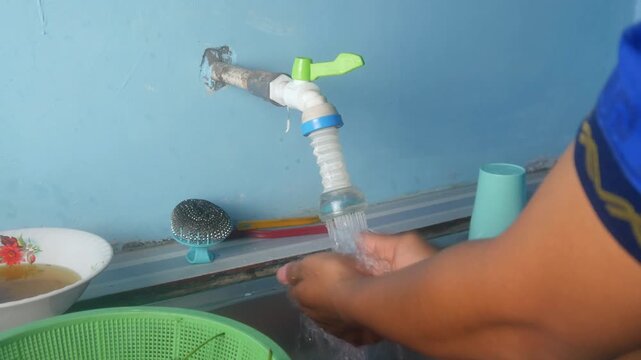 A person's hand turns the lever of the plastic water tap on the kitchen sink.