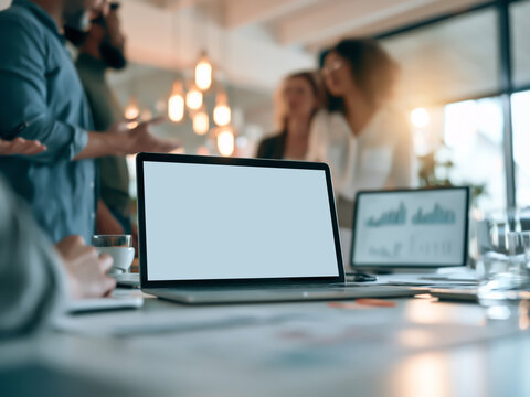 Open laptop with blank white screen mockup on conference table during business meeting in modern office.