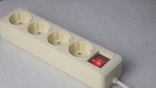 A man's hand is plugging a white charger head into an electrical extension socket.