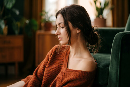 Young woman in orange sweater relaxing on green chair at home