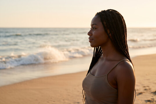 African American young woman gazing at ocean waves at sunset beach