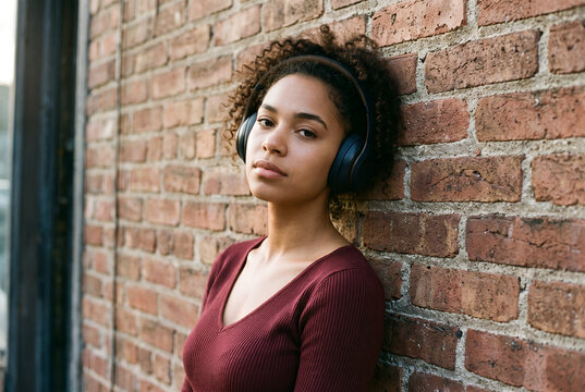 Young African American woman wearing headphones against brick wall