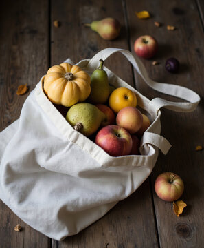 Fresh organic apples pears and yellow pumpkin inside eco friendly white cotton tote bag on rustic wooden table