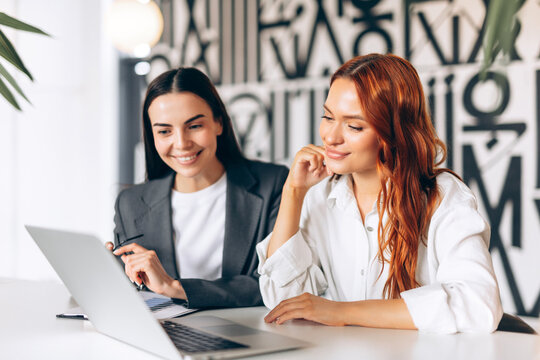 Businesswomen collaborating on laptop, discussing project in modern office