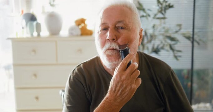 Head shot of a senior man trimming his beard and mustache while looking in the bathroom mirror during his morning grooming routine.