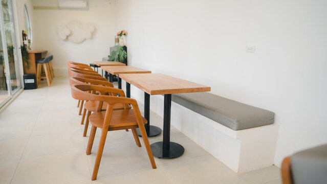 Bright and empty modern cafe dining area with wooden furniture, gray bench cushion, and minimalist white walls. Conceptualizing contemporary retail space, coffee shop, and hospitality.