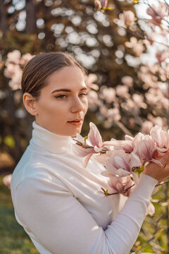 Woman magnolia spring. Serene young woman holding pink blooming magnolia flowers in a sunny garden during springtime.