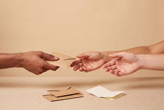Hand passing a kraft envelope to two open waiting hands, giving and receiving, donation and pay it forward