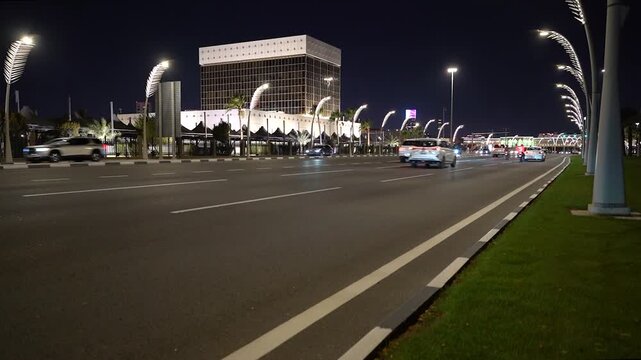 Captivating nighttime automotive b-roll. Vehicles travel along a busy city street illuminated by unique glowing streetlights and a massive, modern government building.