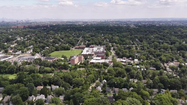 The drone flies forward and tilts down from the suburban horizon toward green athletic grounds, large community buildings and nearby residential streets.