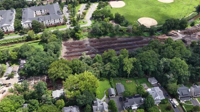 The camera travels laterally from tree lined homes toward community gardens, Cameron Field baseball diamonds and an active construction area near Ridgewood Road.