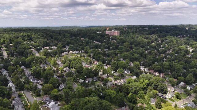 A slow stabilized pan hovers above detached homes, curved streets and dense summer tree canopy in the Maplewood and South Orange area of Essex County.