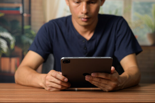 Focused man using tablet device at wooden table in modern home