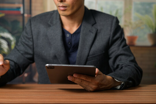 Professional Man Holding Tablet While Sitting at Wooden Table