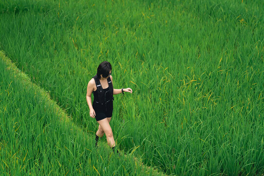 Young woman walking through tall green grass field wearing black sleeveless outfit outdoors in nature