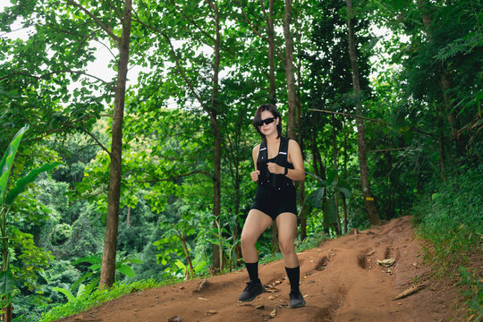 Young woman hiking on a forest trail wearing black shorts, tank top, sunglasses, and backpack during daytime