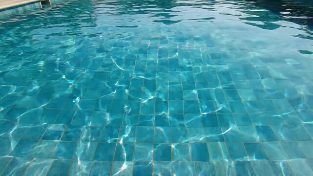 Crystal clear blue water in a tiled swimming pool, with gentle ripples and sunlight reflections dancing on the surface.