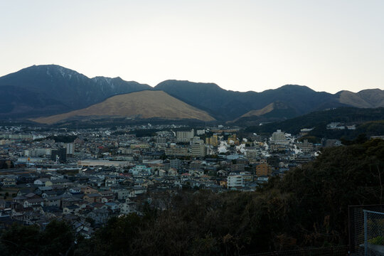 Panoramic wide angle view of Beppu cityscape with geothermal hot spring steam rising against Mount Tsurumi in Kyushu, Japan.