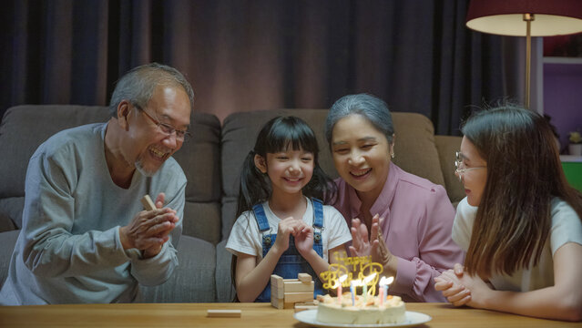 grandparents and mother celebrating enjoy singing birthday song party with cake of granddaughter