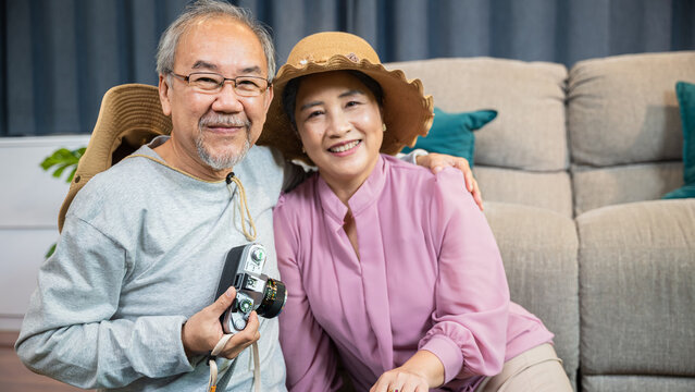 Happy Asian senior couple sitting on the floor preparation next to a suitcase filled with clothes for travelling on weekend trip, old man and woman packing clothes into luggage for journey