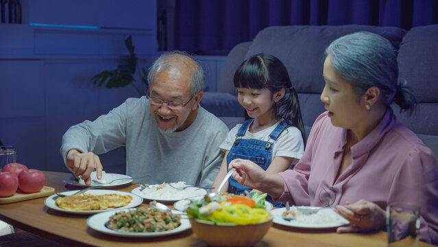 senior parent and child eating dinner food together in living room indoors