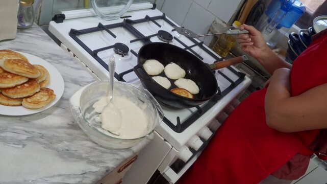 A focused cook flips small pancakes in a hot skillet on a white stove. They feel proud preparing a delicious breakfast. The cozy kitchen feels warm and comforting.