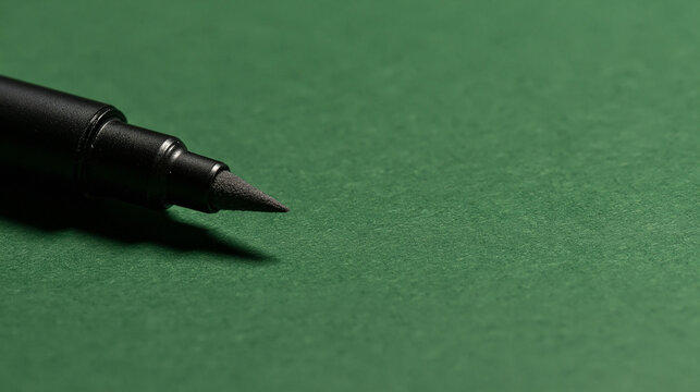 A black pen tip resting on a textured green surface with dramatic side lighting. Perfect for office and creative design projects.
