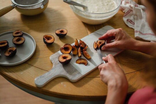 Woman slicing fresh plums on a wooden table, home baking