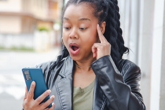 woman on the street making a face of surprise or amazement when she reads a message on her mobile phone