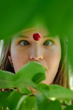 Young woman picking cherries in orchard, crosseyed for fun