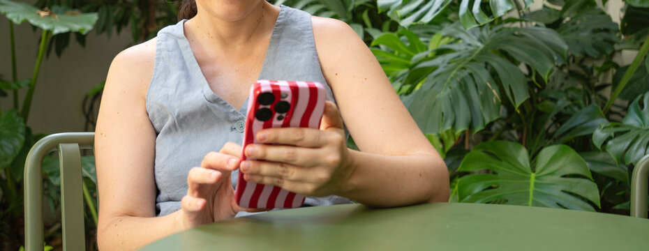 Woman using a smartphone with a striped case while relaxing in a green garden