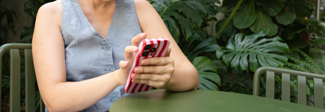 Woman hands holding a smartphone with a striped case, using technology outdoors