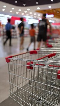 Close-up of empty metal shopping carts with red handles nested together in a row inside a large modern supermarket or hypermarket. Retail trade, consumerism, and shopping concept.