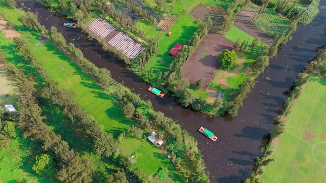 Xochimilco canal crossing with trajineras in the lacustrine area, surrounded by chinampas, wetlands, and multiple trees in the pre-Hispanic area of Mexico City.