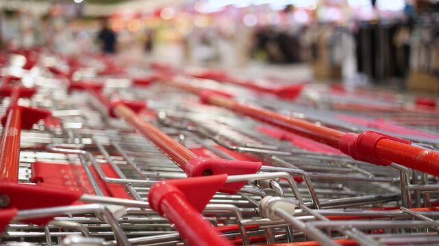 Close-up of empty metal shopping carts with red handles nested together in a row inside a large modern supermarket or hypermarket. Retail trade, consumerism, and shopping concept.