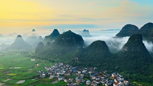 Aerial view of traditional village nestled among misty karst mountain peaks at sunrise in Guilin, China.