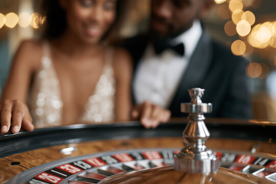Luxury casino night with a smiling couple. Elegant woman in a shimmering gown leans forward. Man in formal attire looks focused and excited. Golden lights blur softly in the background