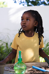 African American female child wearing yellow tee tending soil at garden table with blue trowel © WavebreakMediaMicro