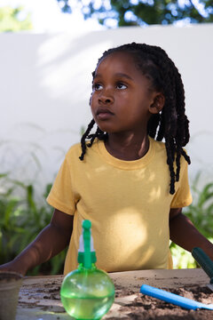 African American female child wearing yellow tee tending soil at garden table with blue trowel
