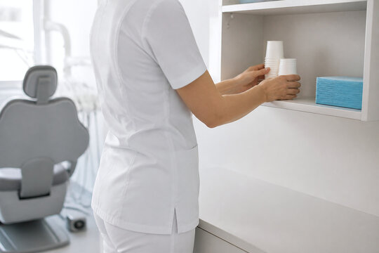 Anonymous Dental Assistant Restocking Disposable Cups and Bibs in Treatment Room