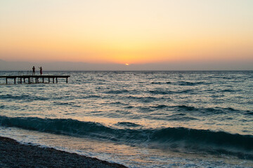 Fototapeta premium silhouette of people walking along the sea beach pier at sunset