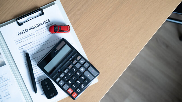 Auto insurance and financial planning concept with red model car, calculator, car key and pen on insurance document with copy space.